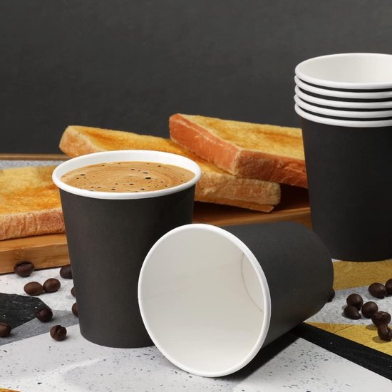 Twee zwarte papieren bekers met koffie, achtergrond met geroosterd brood.