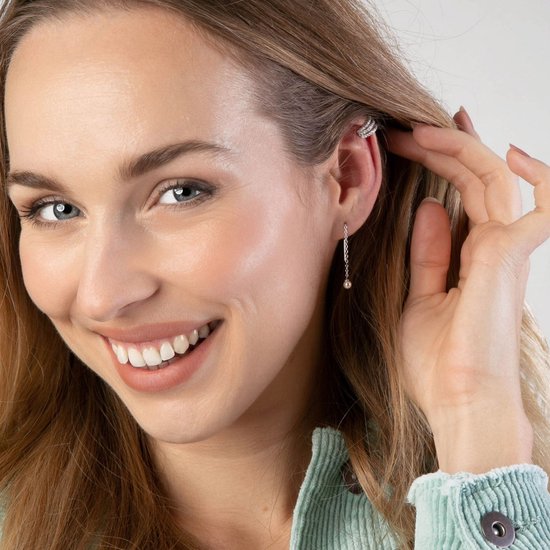 Vrolijke vrouw met lange blonde haren, draagt een zilverkleurige oorclip en oorbel.