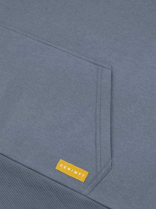 Detail van de kangoeroezak en het gele DENIMFY label op de blauwe hoodie.