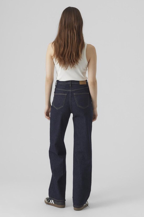 Model van achteren in donkerblauwe wijde jeans, witte top en sneakers.