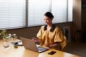Vrouw met nekband speaker zit achter een laptop, lachend.