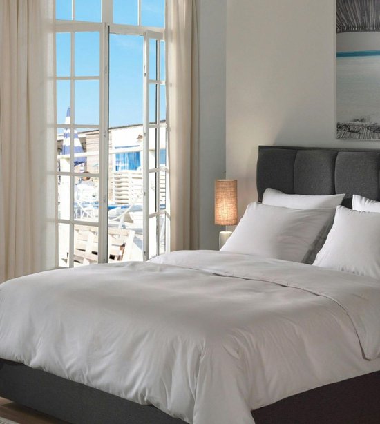 Een opgemaakt bed met Vaporous Grey dekbedovertrek, bij een raam met uitzicht op zee.