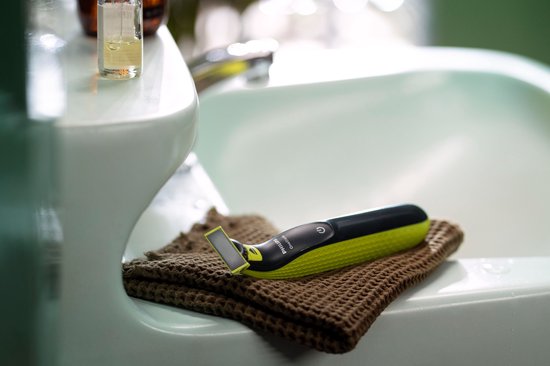 Felgroene en zwarte OneBlade scheerapparaat ligt op een bruine handdoek naast een wastafel.