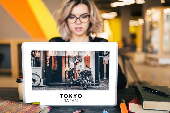 Une femme portant des lunettes regarde un ordinateur portable avec un autocollant d'une scène de rue de Tokyo avec un vélo.