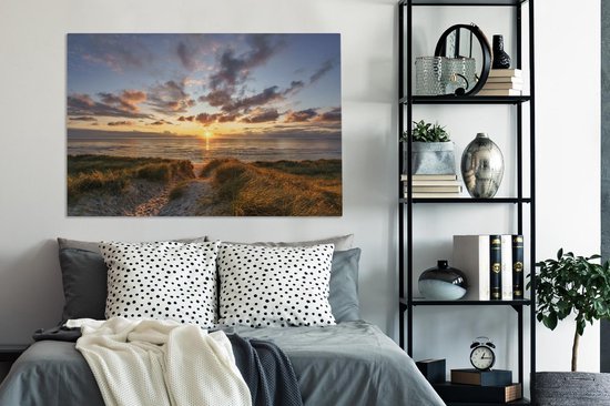 Chambre à coucher avec un lit gris et sur le mur une toile d'un coucher de soleil sur les dunes.