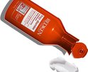 Flacon d'après-shampooing Redken Frizz Dismiss ouvert. Une crème blanche est à côté.