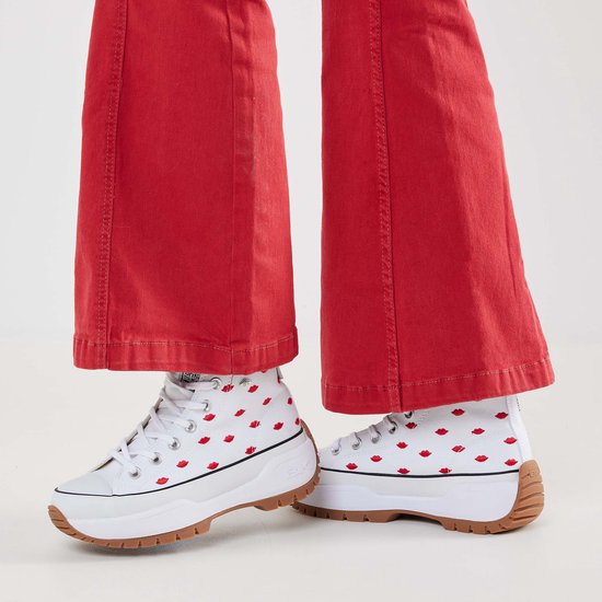 Witte hoge sneakers met rode lippenprint, gedragen met rode broek.