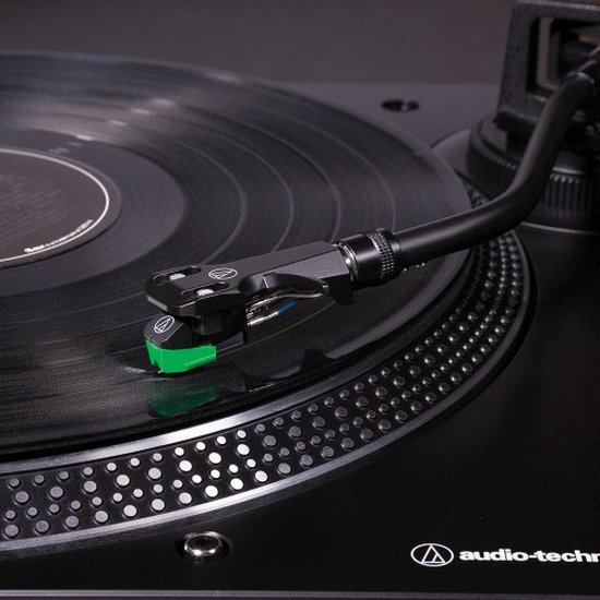 Close-up van een zwarte toonarm met een groene naald die op een draaiende vinylplaat rust.