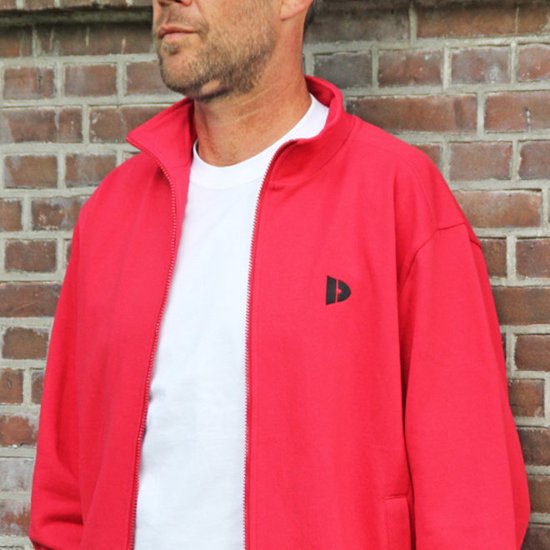 Close-up van een man met rood trainingsvest met rits en zwart logo, met witte T-shirt eronder.