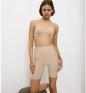 Een vrouw knielt op een kruk, draagt een huidkleurige beha met kanten details en een bijpassende shapewear short tot op de knie.