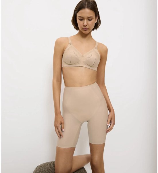 Een vrouw knielt op een kruk, draagt een huidkleurige beha met kanten details en een bijpassende shapewear short tot op de knie.