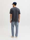 Man met donkergrijs t-shirt, blauwe jeans en pet, staand met rug naar de camera.