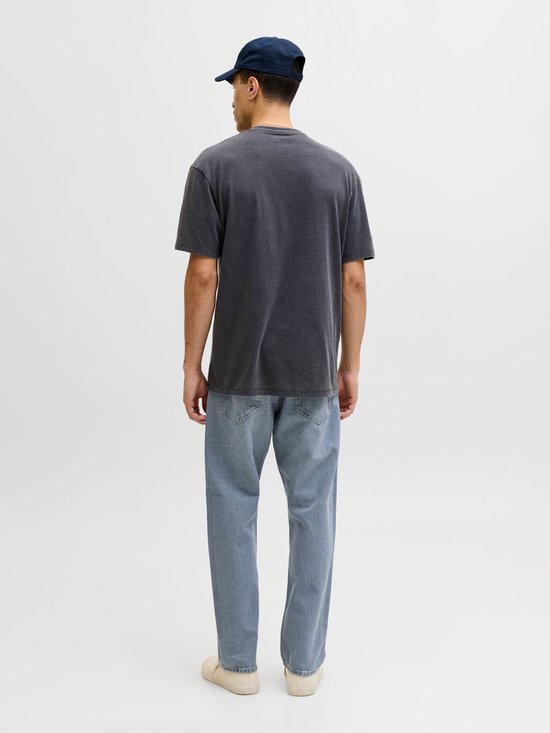 Man met donkergrijs t-shirt, blauwe jeans en pet, staand met rug naar de camera.