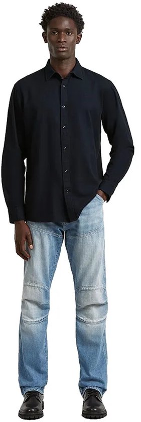 Man, hele lichaam, draagt een donkerblauw regular fit overhemd en lichte jeans, op witte achtergrond.