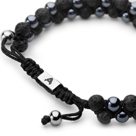 Detail van een dubbele armband met zwarte en grijze kralen, met een zilverkleurige A-bedel aan een zwart koord.