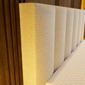 Close-up van het gestreepte beige hoofdbord van de boxspring, met een matras met honingraatpatroon.