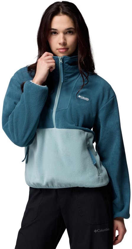 Model draagt een blauwe fleece trui met halve rits en lichtblauwe onderkant. Ze houdt de kraag vast.