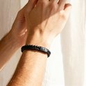 Zwarte gevlochten lederen armband met kralen van zwarte lavasteen en mat zwart, gedragen om een mannenpols.