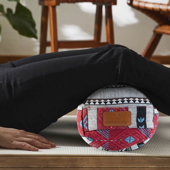 Femme allongée sur un tapis avec un bolster à motif géométrique rouge, blanc et bleu sous ses genoux.