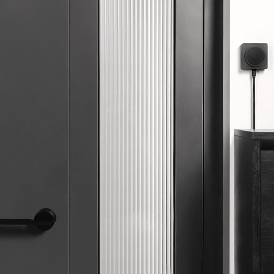 Zwarte vierkante chime met grill aan de muur naast een donkere deur.