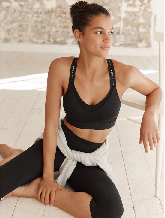 Model draagt zwarte sportbeha en legging, met een grijze trui om de middel.