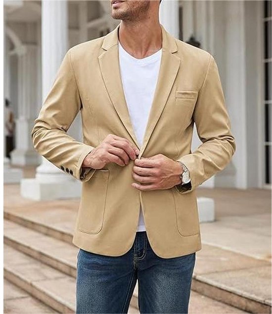 Man in een lichtbruine casual blazer met één knoop, spijkerbroek en wit T-shirt. De blazer heeft twee klepzakken en knopen op de mouwen.
