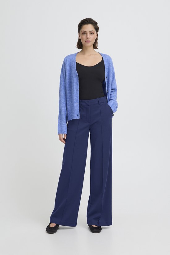 Model in een donkerblauwe, wijde broek met rechte pijpen, hoge taille, gecombineerd met een zwarte top en blauw vest.