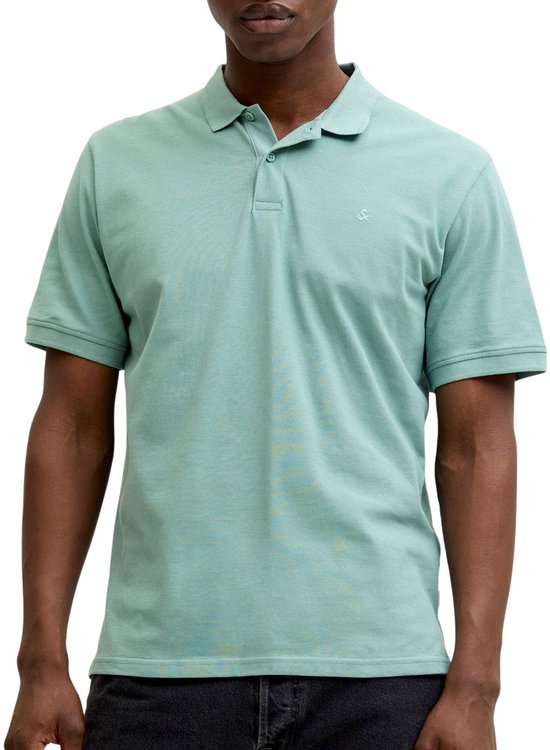 Un homme porte un polo vert menthe à manches courtes avec un logo brodé sur la poitrine.