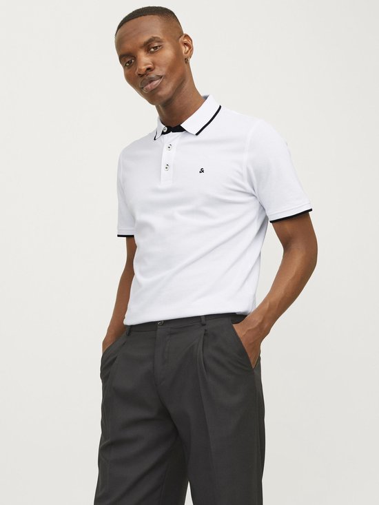 Man draagt een wit poloshirt met zwarte bies en donkere broek.