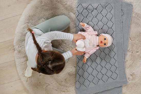 Meisje speelt met baby pop in roze pyjama op grijze deken. Baby Annabell.