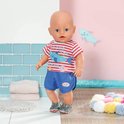 Baby Born pop staand, met rood-wit gestreept shirt met haai en blauwe broek. Draagt grijze haaienschoentjes.
