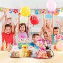 Kinderen met ballonnen op een verjaardagsfeestje, met op de voorgrond stapels gekleurde snoepjes in organzazakjes.