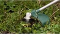 Grastrimmer kop die brandnetels snijdt met een groene beschermkap.