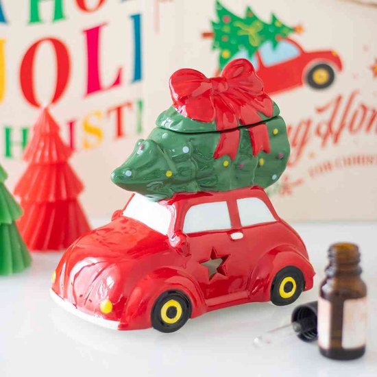 Rode auto met groene kerstboom en rode strik, naast kerstboomdecoraties en een olieflesje.