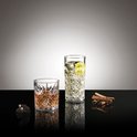 Deux verres à motif losange sur une table noire : un verre bas avec une boisson ambrée et un grand verre avec une boisson jaune et une tranche de kiwi.