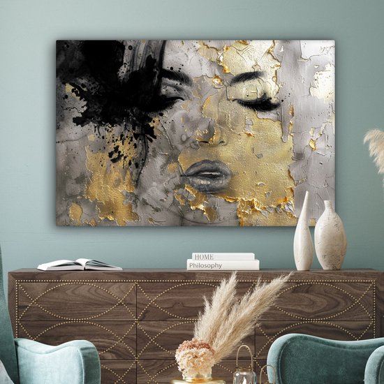 Abstract schilderij van een gezicht met zwarte verfspatten en gouden accenten, boven een dressoir met decoratie.