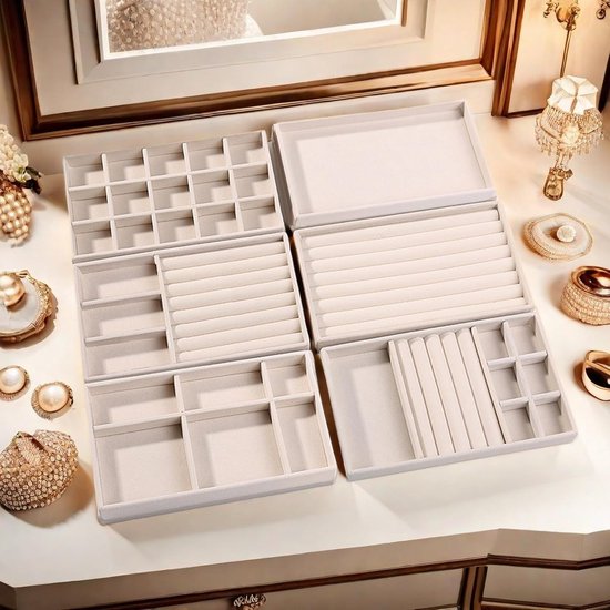Lege, beige, stapelbare sieradenorganizers met verschillende vakverdelingen op een witte tafel.