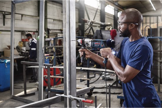 Un homme fore un profil métallique avec une perceuse Bosch bleue.