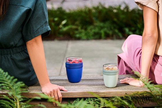 Twee vrouwen buiten, een met een blauwe en een met een groene Mepal lunchpot gevuld met fruit en muesli.