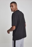 Man draagt zwart oversized T-shirt, met de rug naar de camera gedraaid, kijkt over de schouder. Grijze joggingbroek met zwarte streep.