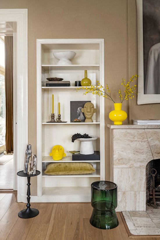 Een interieur met een boekenkast vol decoraties, waaronder gele vazen, kandelaren en beeldjes.