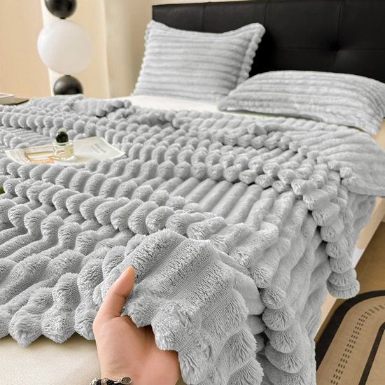 Hand die een lichtgrijze, geribbelde fleece deken vasthoudt op een bed met kussens.