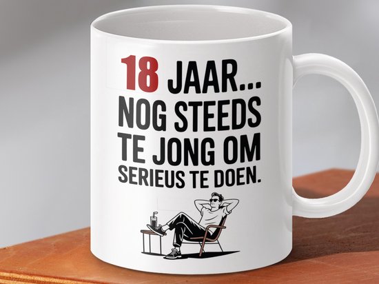 Witte mok met tekst "18 JAAR... NOG STEEDS TE JONG OM SERIEUS TE DOEN." en illustratie van een relaxte man in een stoel.
