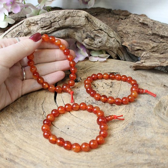 Hand met drie oranje carneool armbanden met rode draden op hout