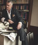Man met gestreept pak en wit overhemd, zittend bij een boekenkast, met een kopje thee.