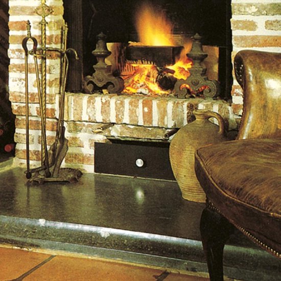 Gezellige open haard met brandend vuur, antiek haardgereedschap, een vaas en een leren stoel.