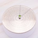 Collier argenté avec un unique zircon vert sur une surface argentée.