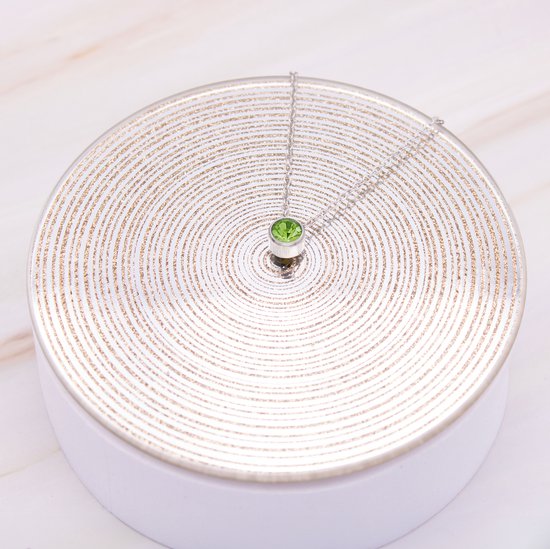 Collier argenté avec un unique zircon vert sur une surface argentée.