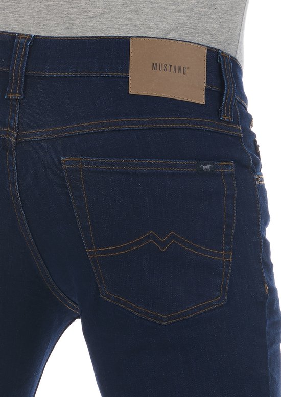 Close-up van de achterkant van een donkerblauwe jeans met oranje stiksels, Mustang-label en een klein paardlogo.