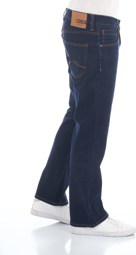 Man in donkerblauwe bootcut jeans met oranje stiksels en witte sneakers.